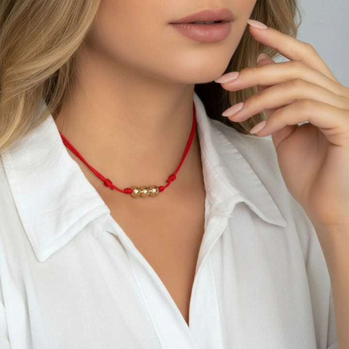 Woman wearing a red necklace with gold beads against a neutral background