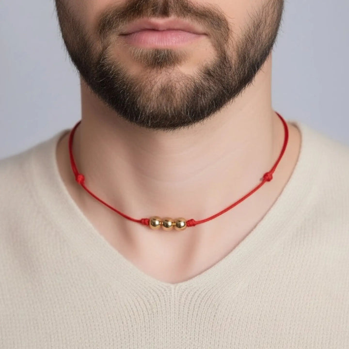 Man wearing a red necklace with solid gold beads against a neutral background