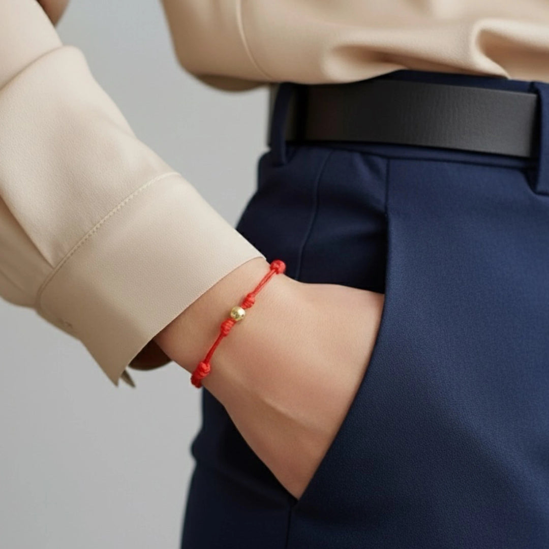 Person wearing a red solid gold bead bracelet on a plain background
