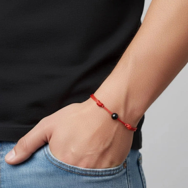 Person wearing a red bracelet with a black tourmaline bead on a plain background