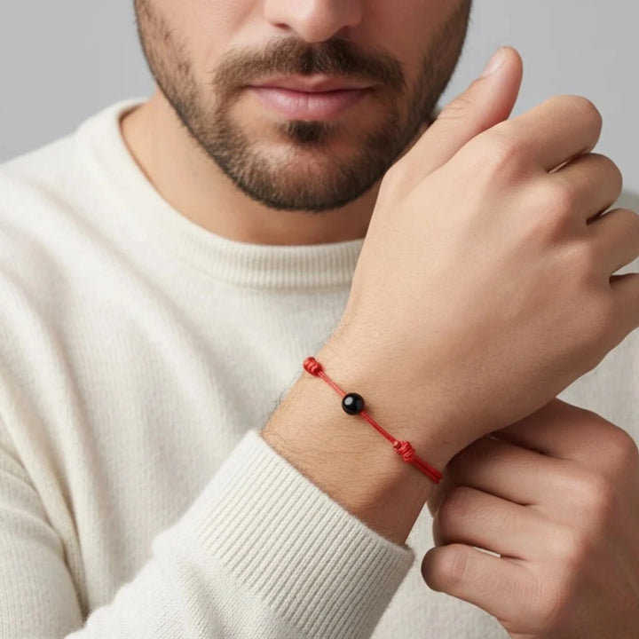 Man wearing a red bracelet with a black tourmaline bead on his wrist.