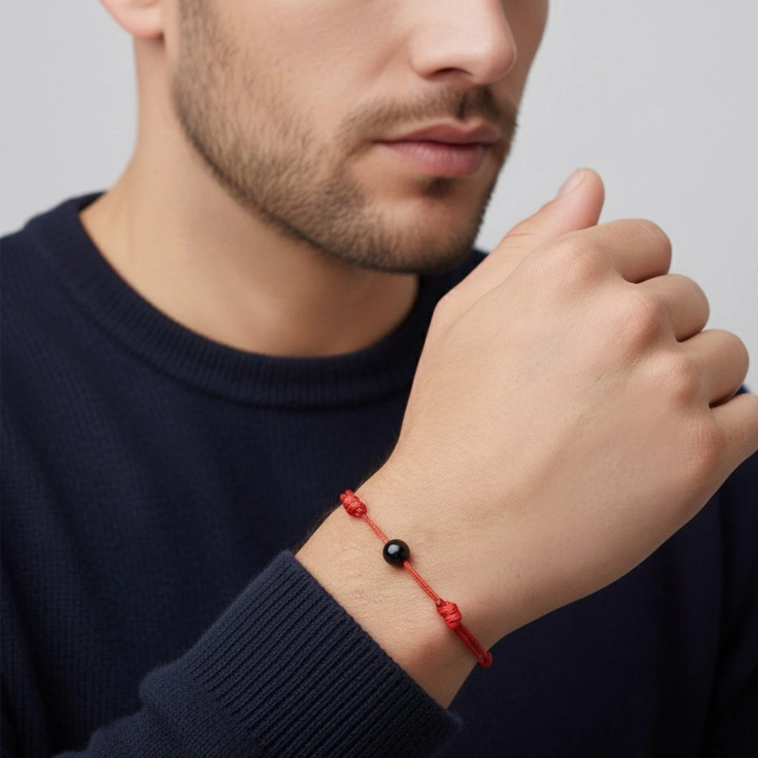 Man wearing a red bracelet with a black tourmaline bead on a plain background