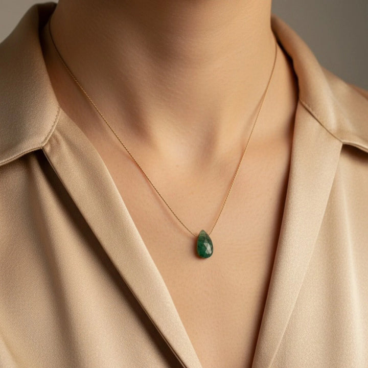 Necklace with a green emerald pendant worn by a person in a beige shirt.