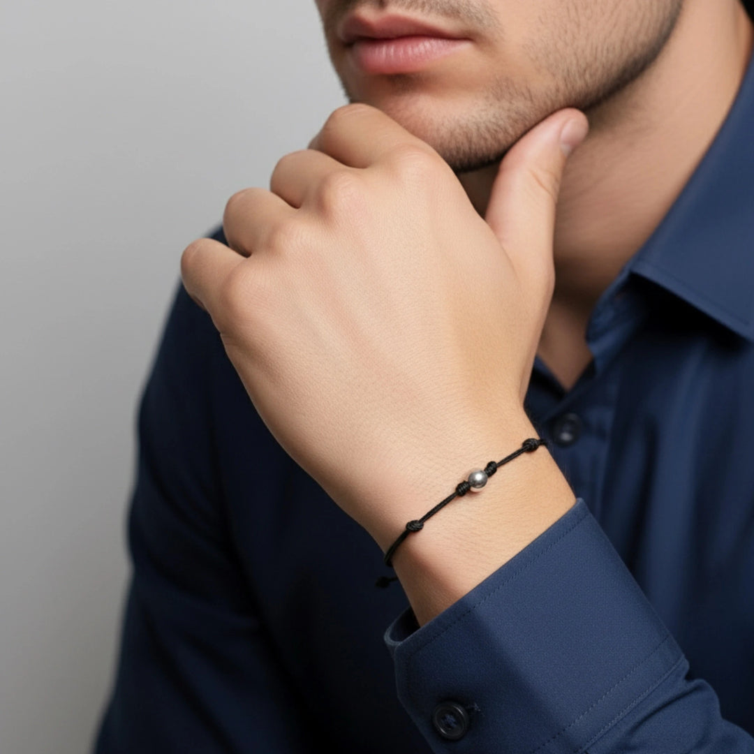 Person wearing a black solid gold beaded bracelet on a plain background