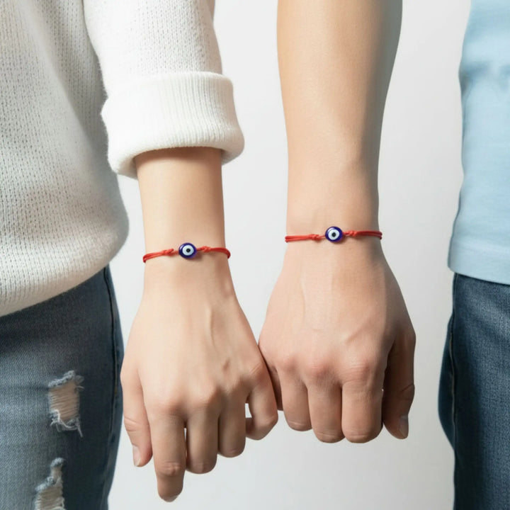 Two people wearing red bracelets with blue evil eye designs on a plain background
