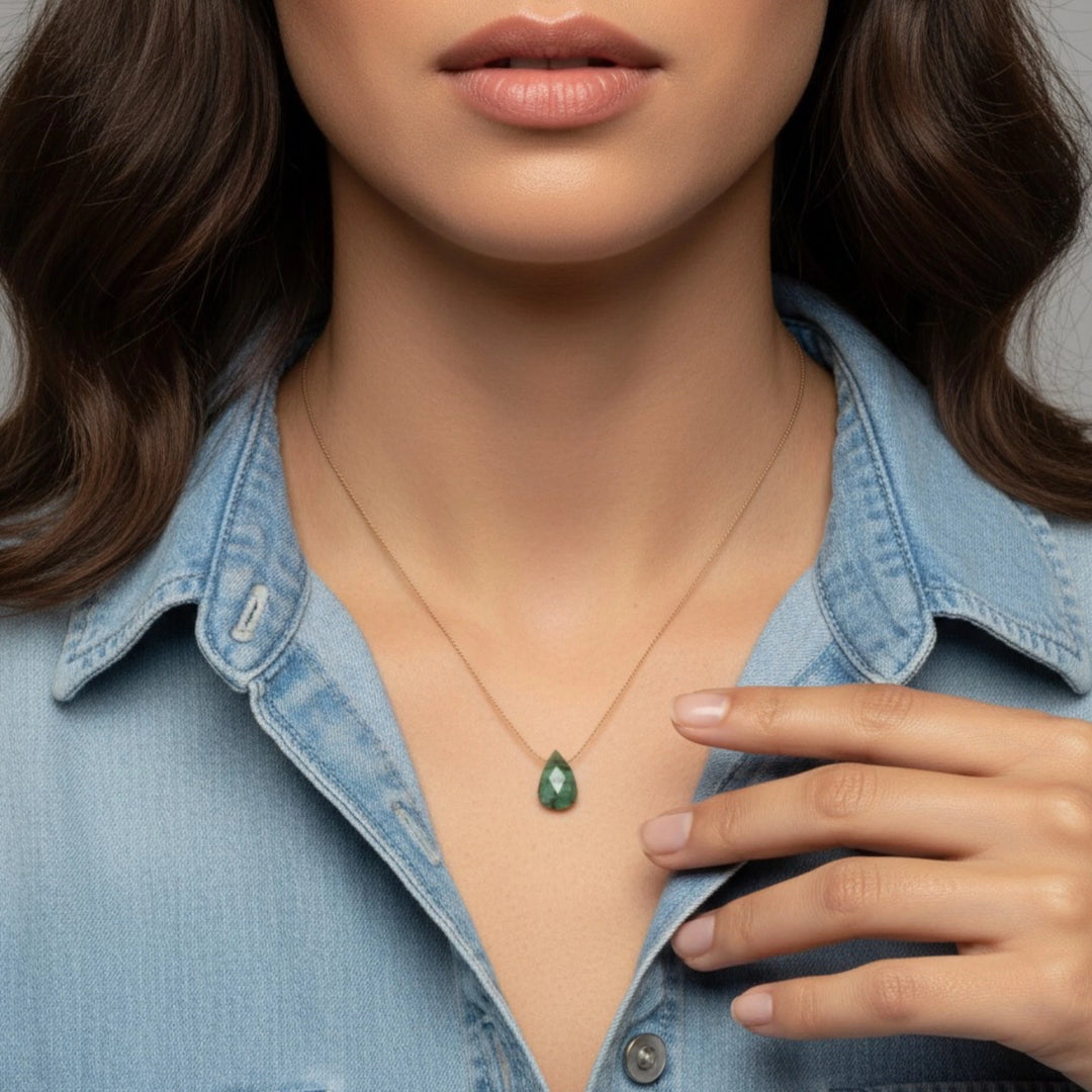 Woman wearing a green emerald teardrop pendant necklace with a denim jacket.