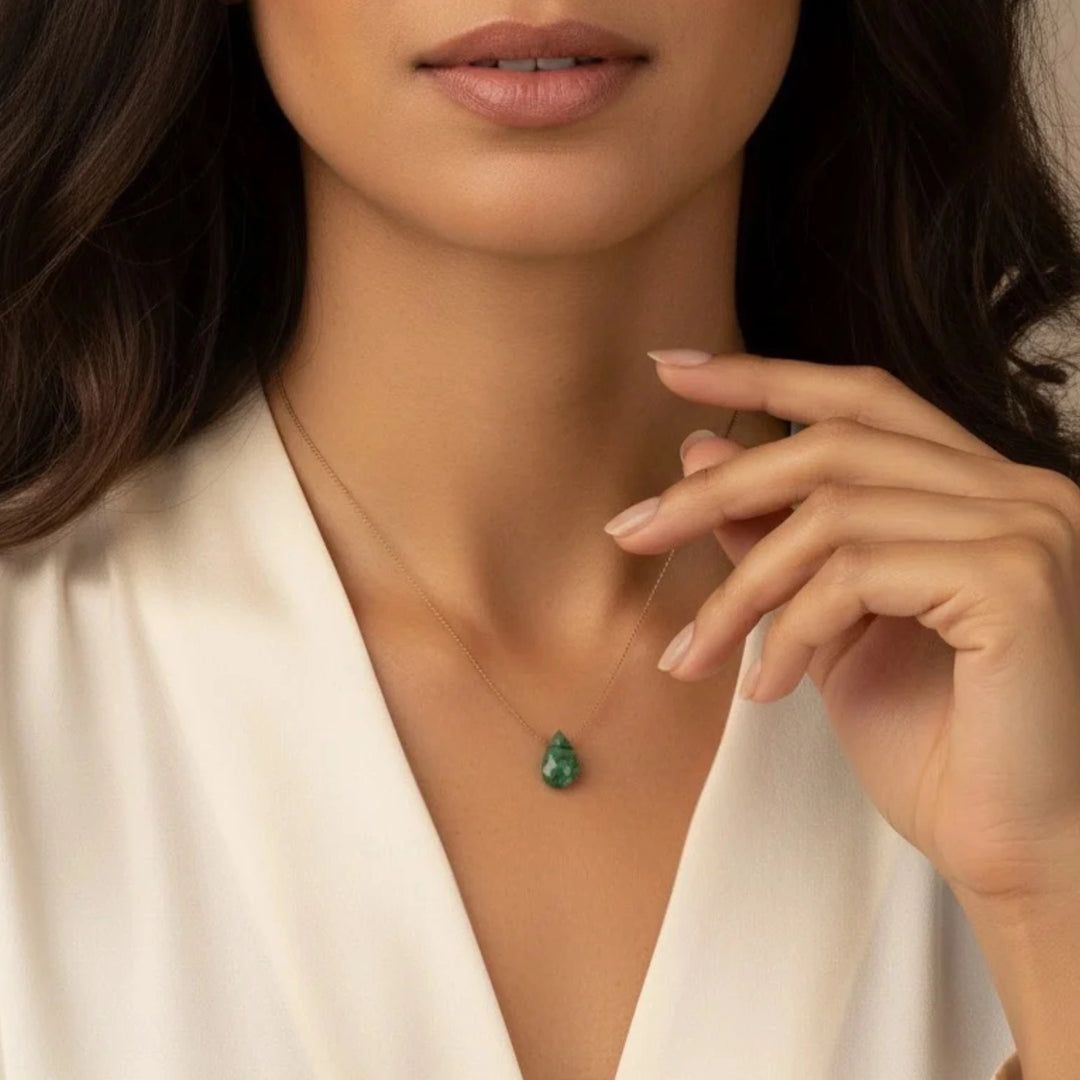 Woman wearing a necklace with a green emerald pendant, close-up on neck and hand.
