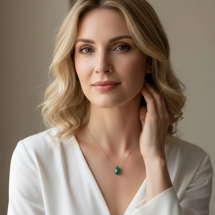 Woman wearing a white top and green emerald necklace against a neutral background