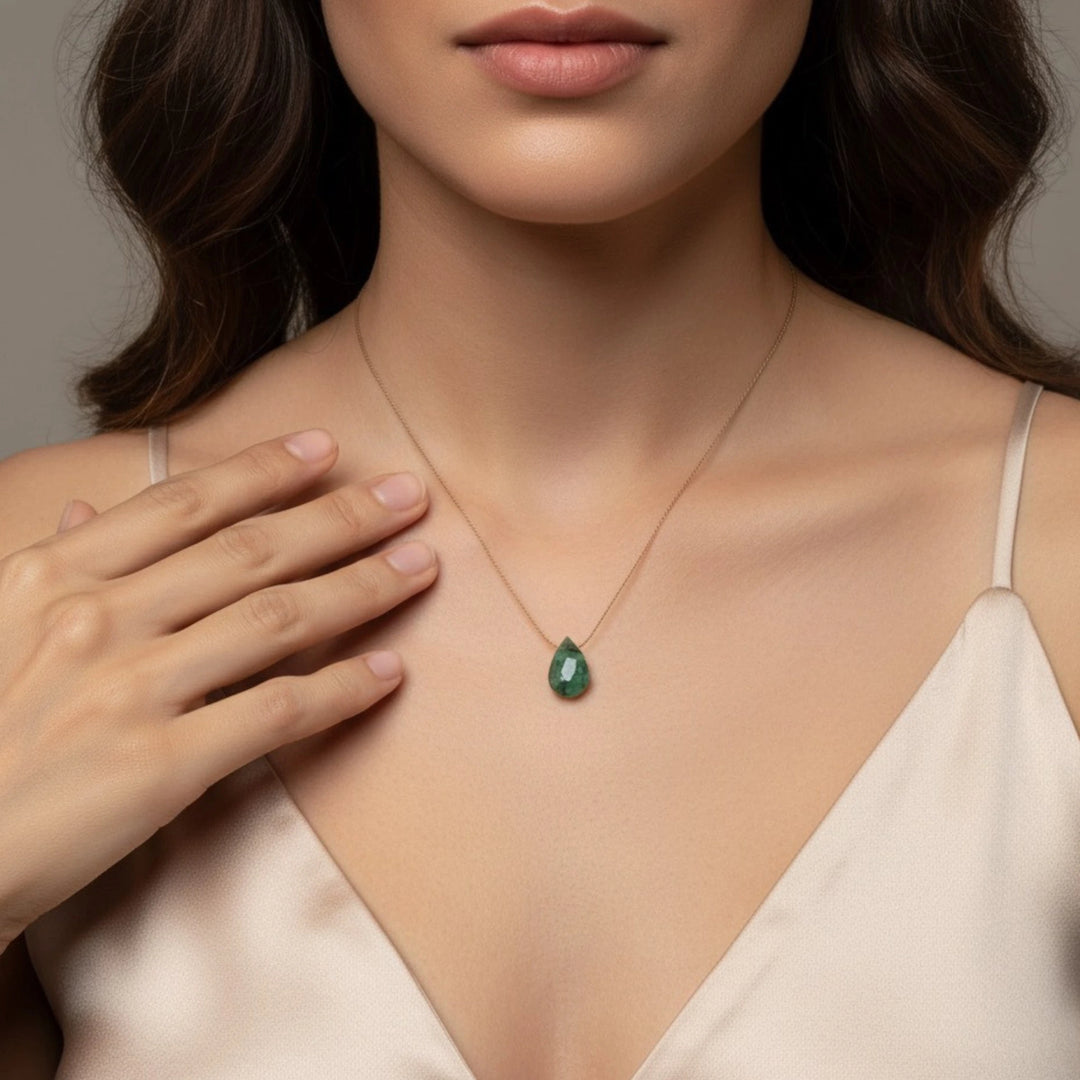 Woman wearing a necklace with a green emerald pendant, hand on chest