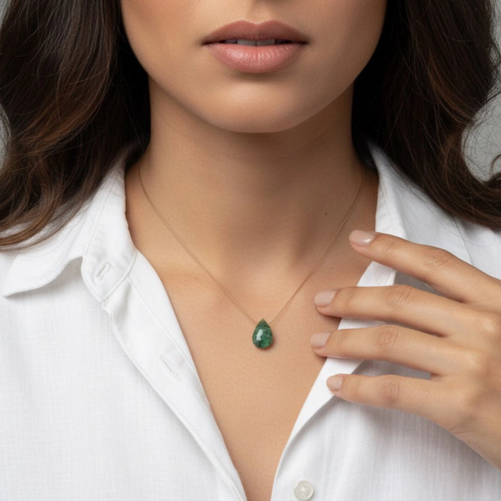 Woman wearing a necklace with an emerald pendant against a white shirt background