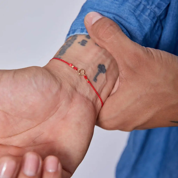 Luck Strings red string bracelet with 14k solid yellow gold clasp on a person's wrist.