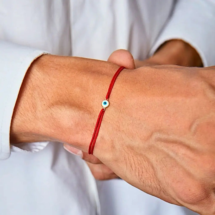 A person's wrist wearing a 14K gold vermeil evil eye link connector on a red string bracelet.