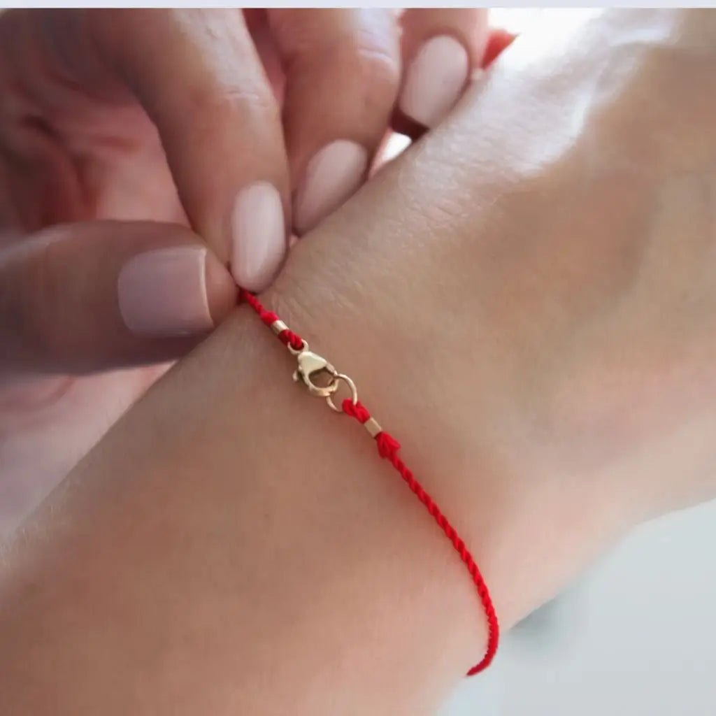 Luck Strings red string bracelet with 14k solid yellow gold clasp on a person's wrist.