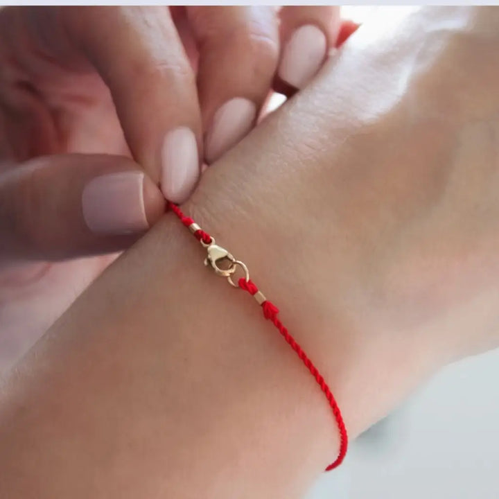 Luck Strings red string bracelet with 14k solid yellow gold clasp on a person's wrist.