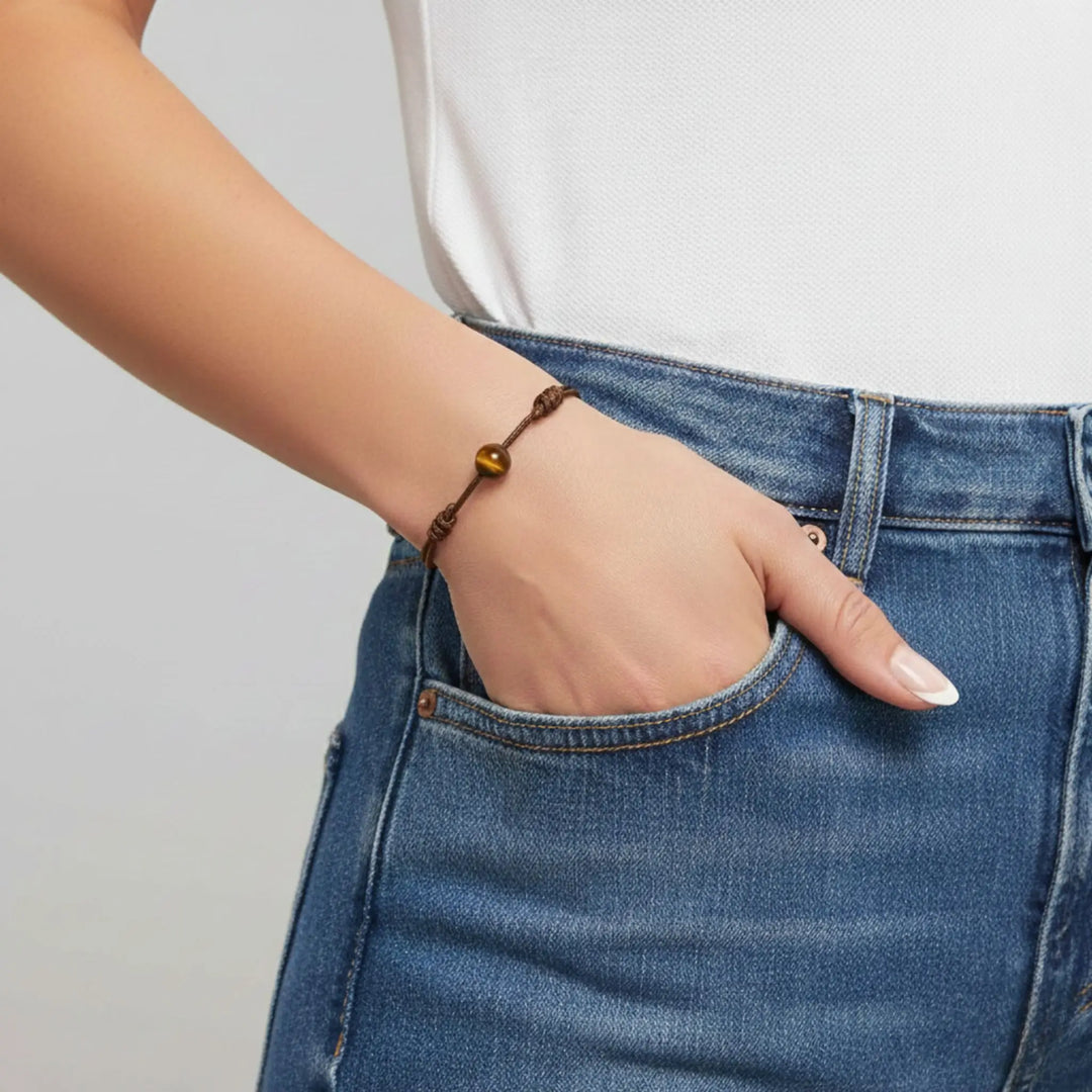 Person wearing blue jeans with a tiger eye bracelet on a plain background