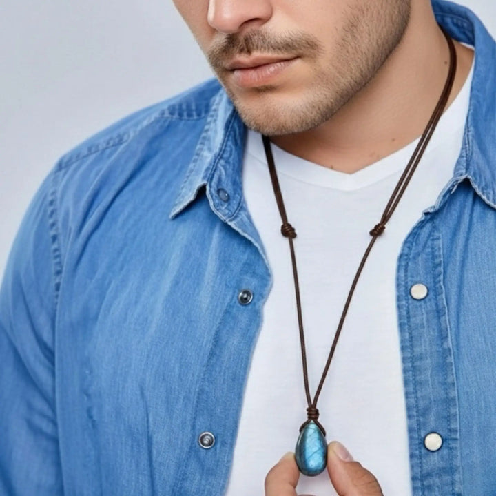 Man wearing a blue denim jacket holding a necklace with a flash blue labradiorite pendant.