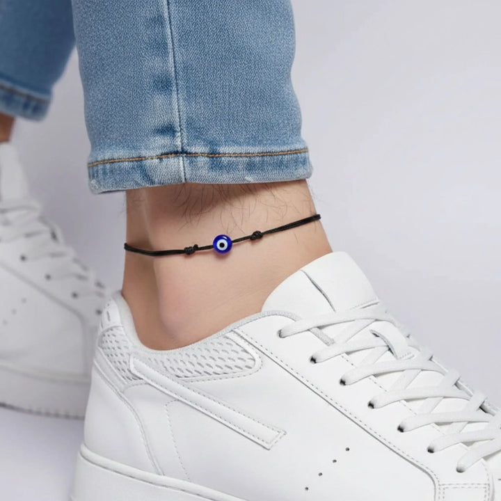 Ankle bracelet with a blue bead worn on a person's ankle, with white sneakers and light blue jeans.
