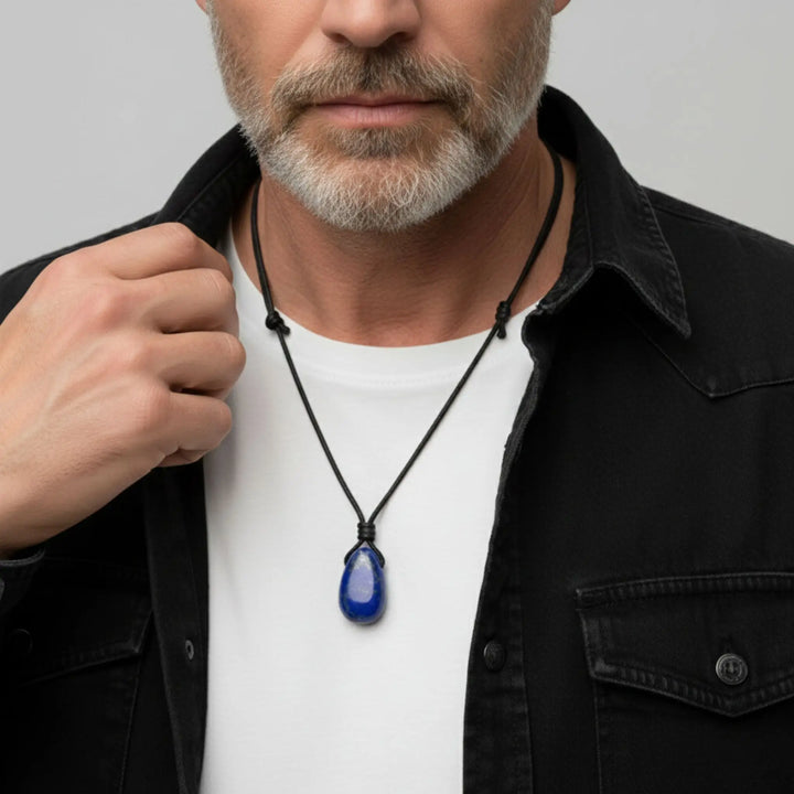 Man wearing a black jacket with a white shirt and a necklace with a blue lapis lazuli  pendant.