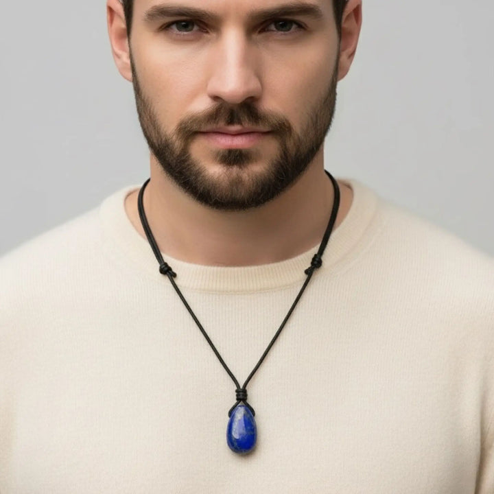 Man wearing a necklace with a blue lapis lazuli pendant against a plain background