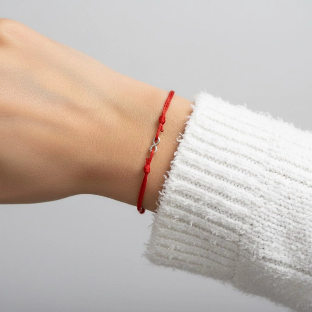Red bracelet on a wrist with a white sleeve against a gray background