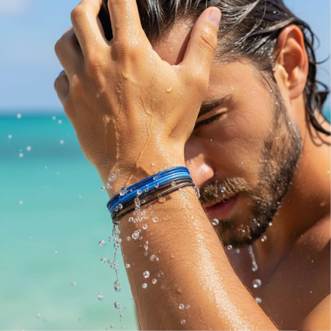 Man with wet hair and water droplets, wearing a blue wristband, against a beach background.