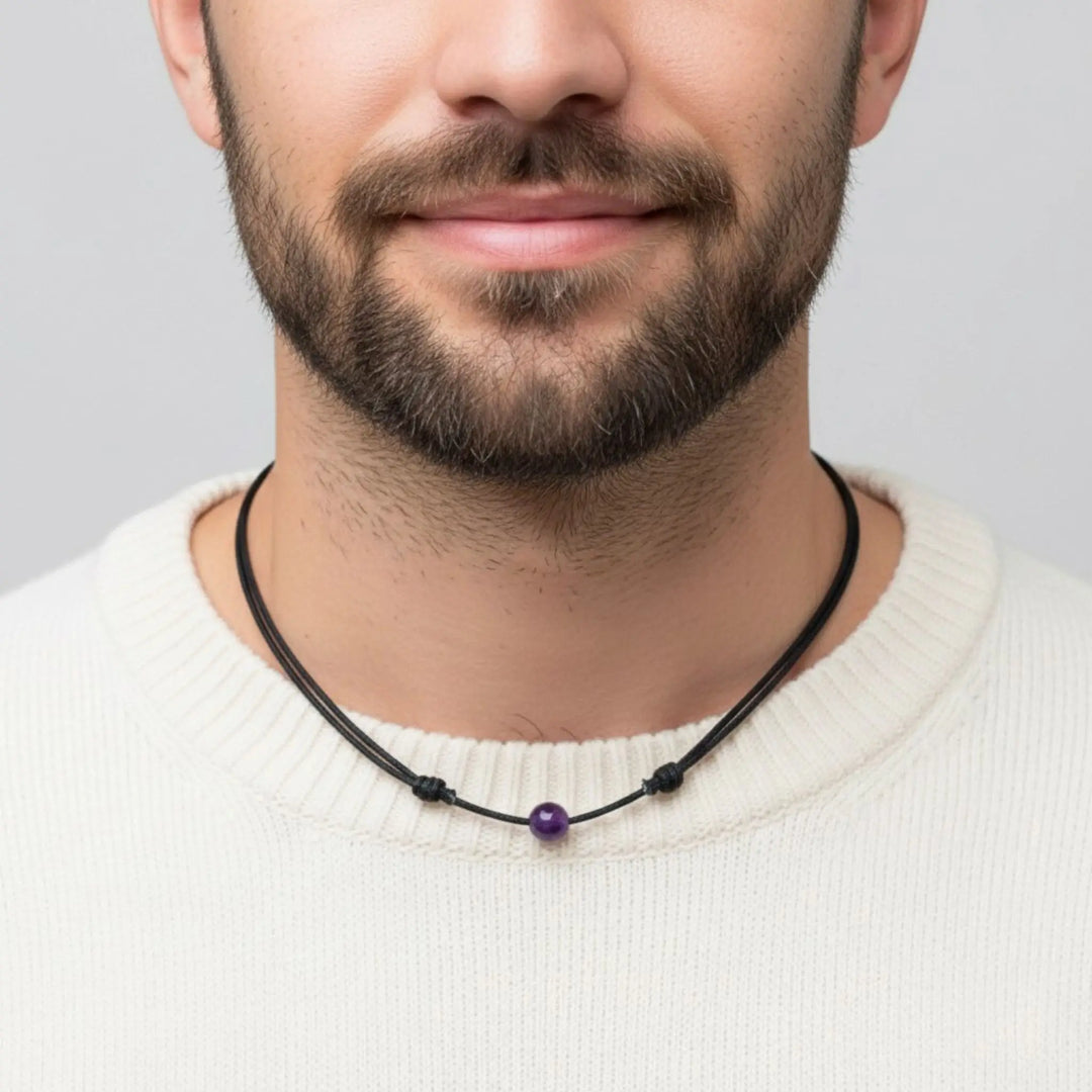 Man wearing a black beaded necklace with a amethyst purple bead on a plain background