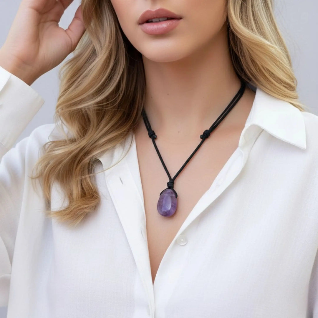Woman wearing a necklace with a purple amethyst pendant against a neutral background