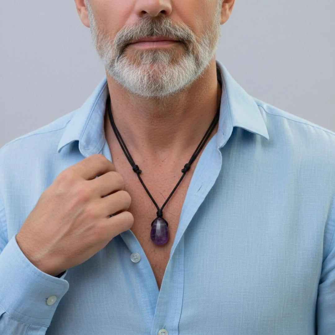 Man wearing a light blue shirt with a necklace featuring a purple amethyst pendant against a plain background