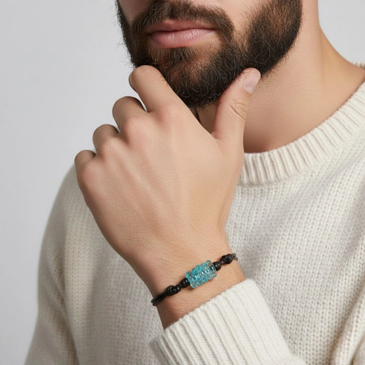 Person wearing a bracelet with a blue glass bracelet on a plain background