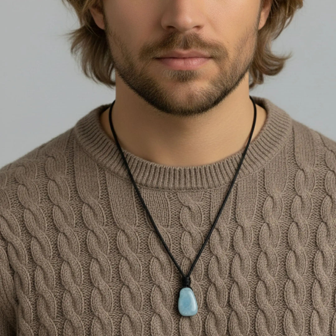 Man wearing a brown cable knit sweater with a necklace featuring a blue pendant.