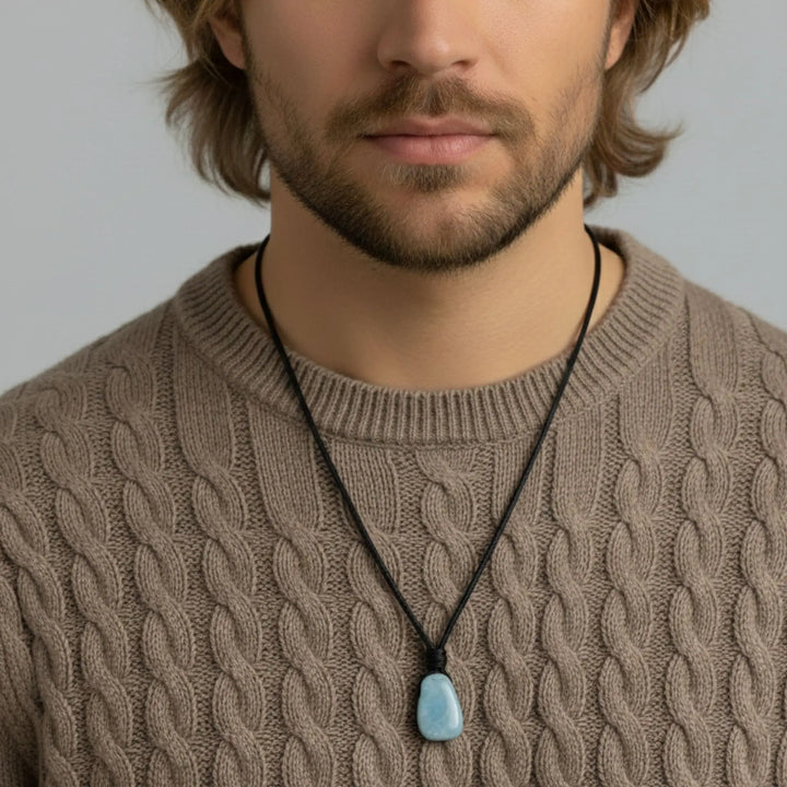 Man wearing a brown cable knit sweater with a necklace featuring a blue pendant.