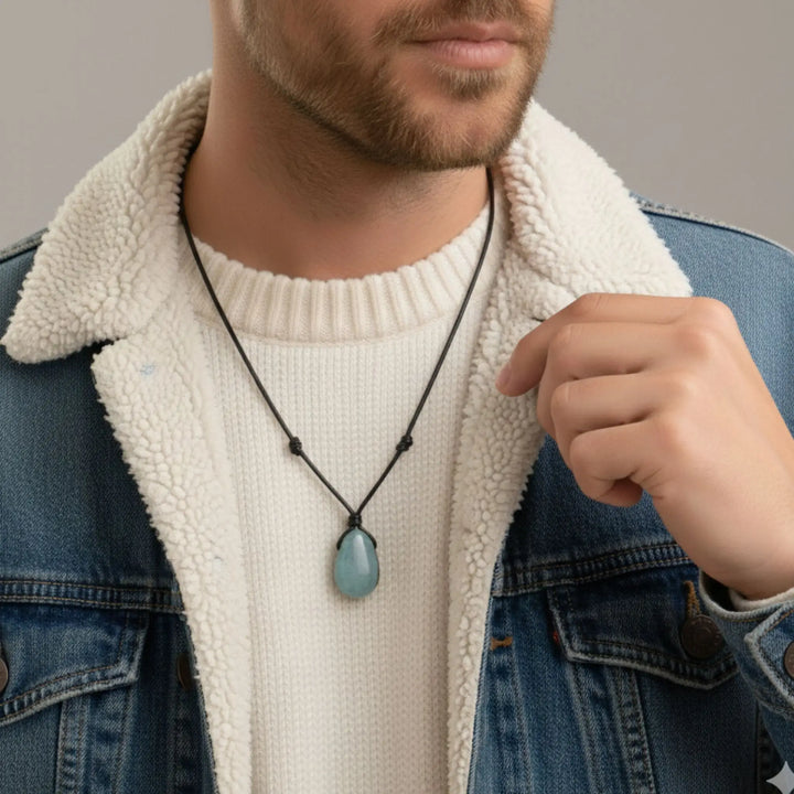 Man wearing a necklace with a blue aquamarine pendant, pointing to it.