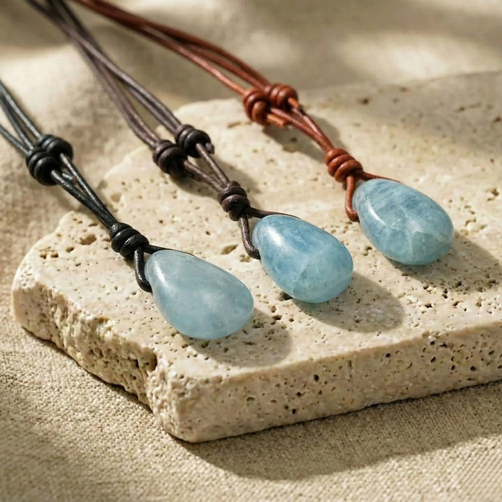 Three necklaces with blue aquamarine drop pendants on a stone surface