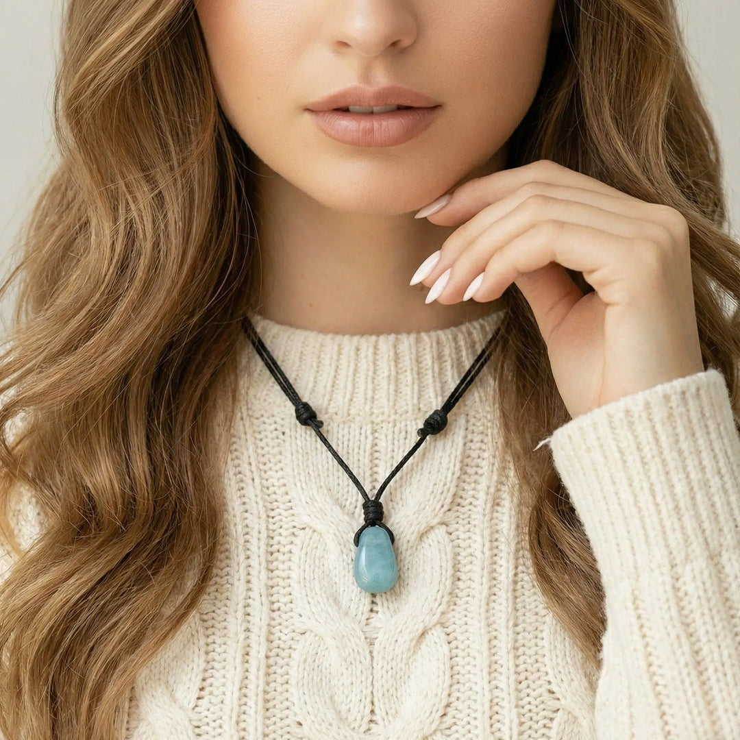 Woman wearing a necklace with a blue aquamarine pendant, wearing a beige sweater.