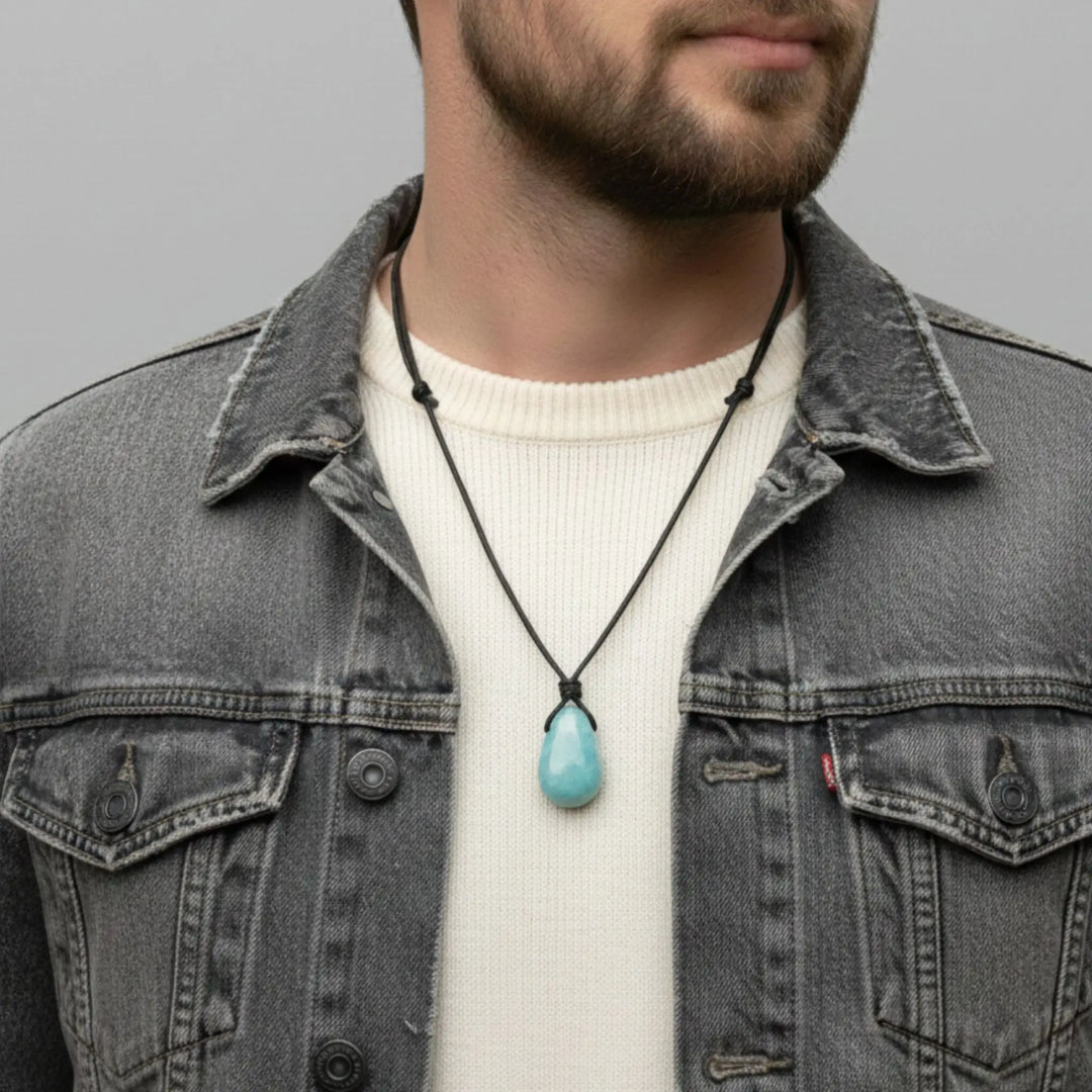 Man wearing a denim jacket with a necklace featuring a aquamarine pendant against a gray background
