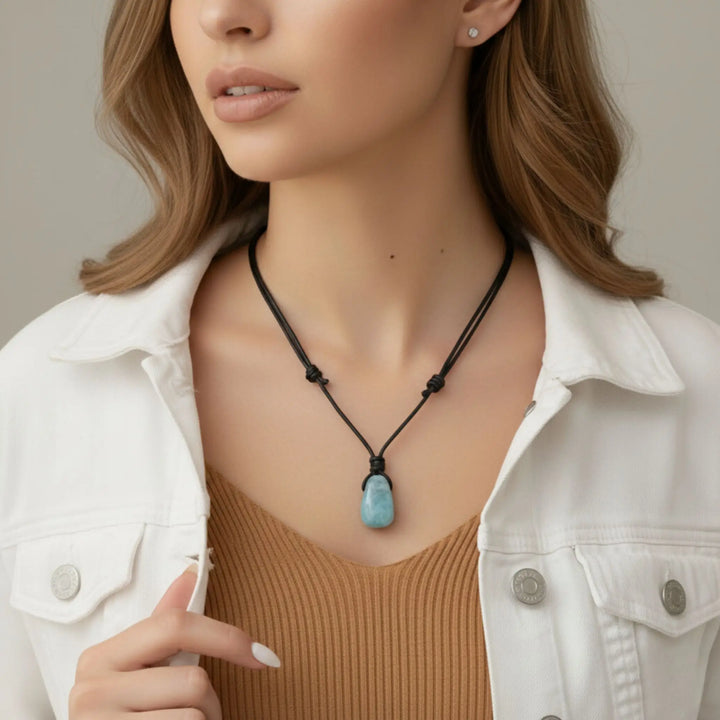 Woman wearing a necklace with a blue aquamarine pendant against a neutral background
