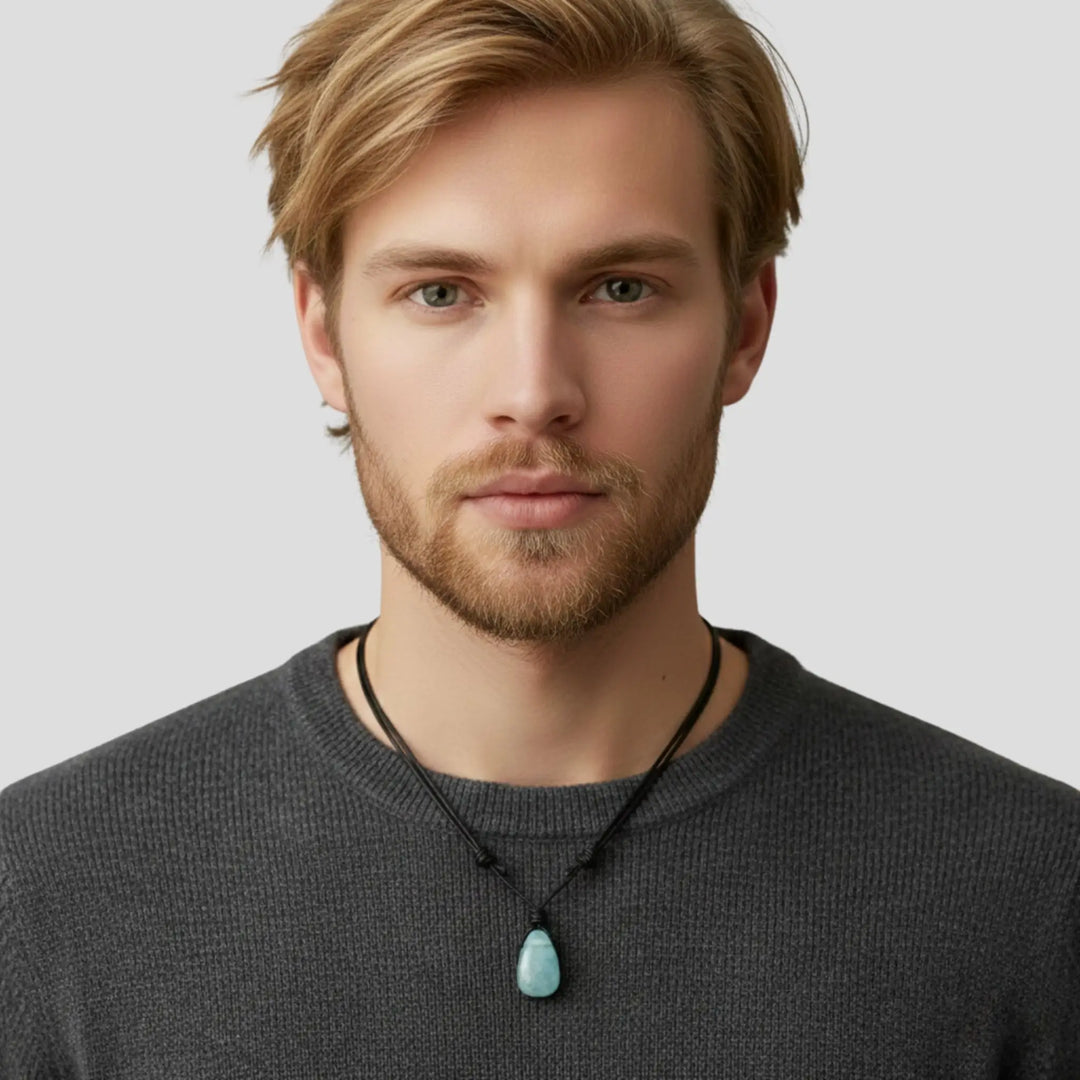 Man wearing a gray sweater with a turquoise pendant necklace on a light gray background