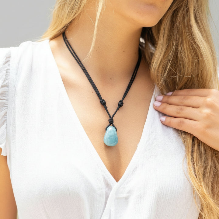 Woman wearing a necklace with a blue aquamarine pendant against a neutral background