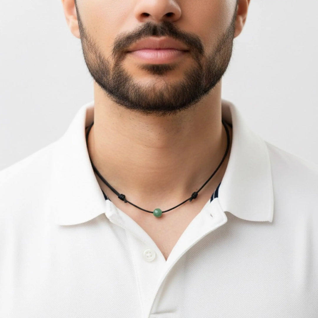 Man wearing a white shirt with a black necklace featuring a green aventurine bead on a light gray background