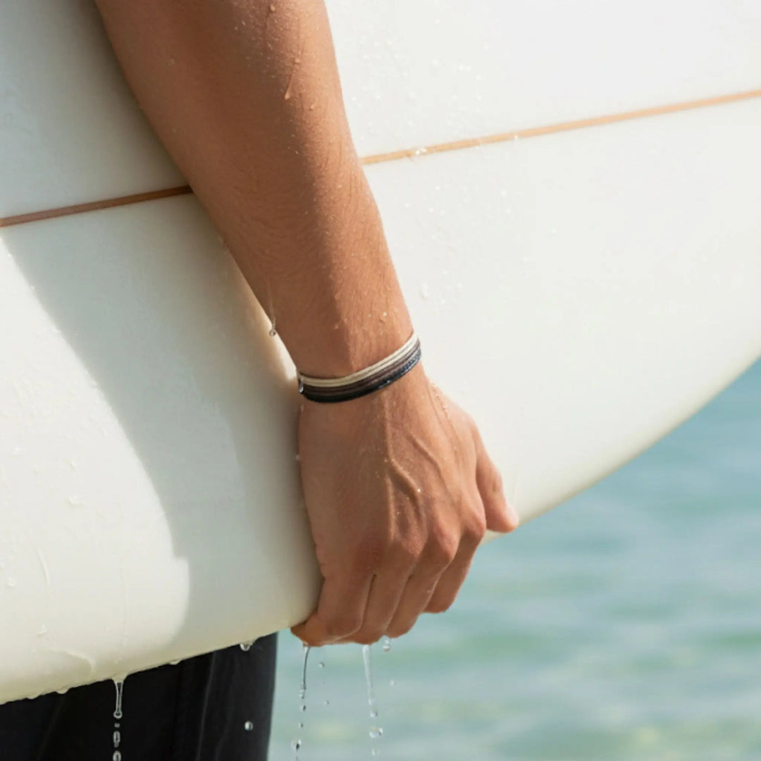 Person holding a surfboard with water droplets, blurred ocean background