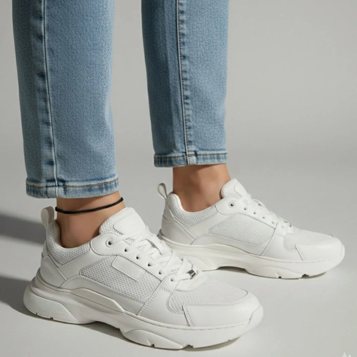 Black anklet styled with white sneakers and light blue jeans on a gray background.