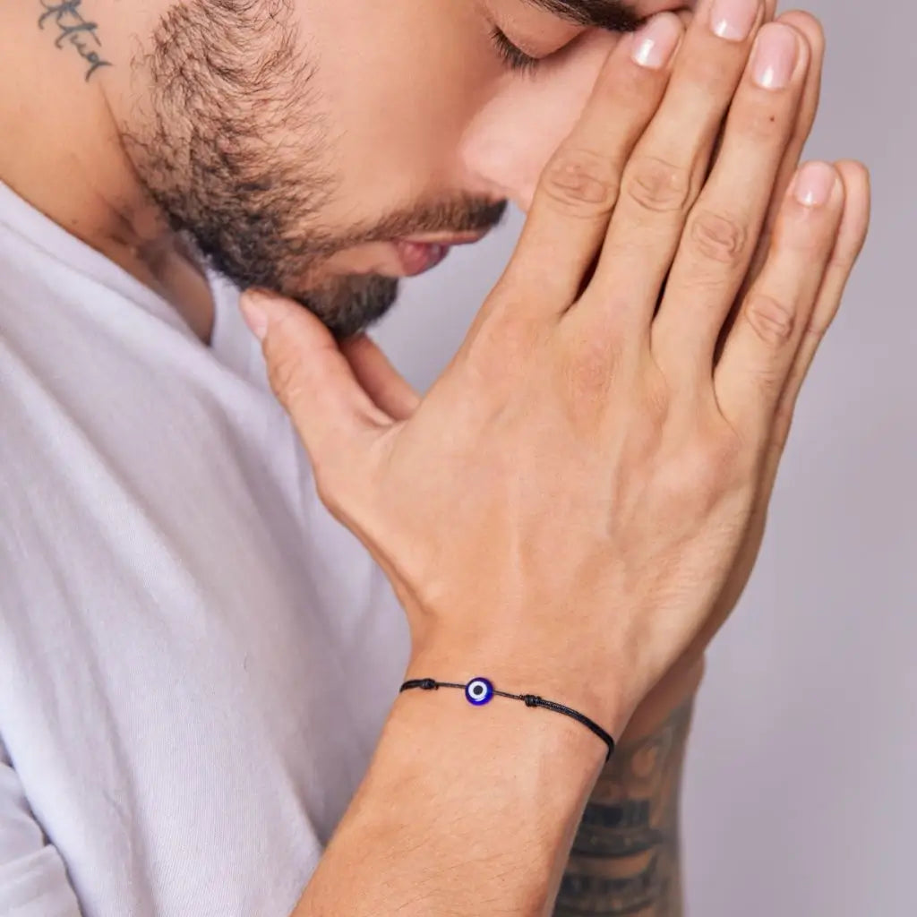 Praying hands wearing black string bracelets with evil eye charms, perfect for couples - Luck Strings.