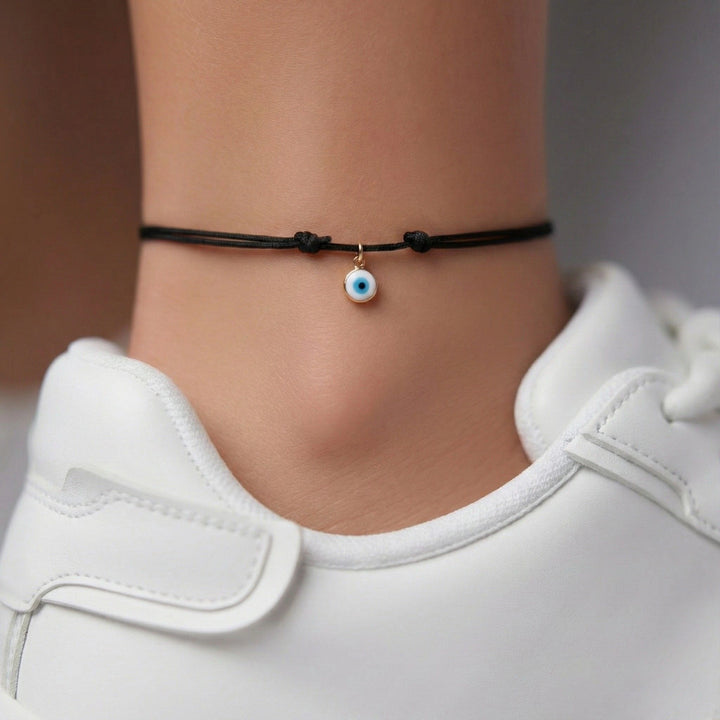 Black cord bracelet with a blue evil eye charm on a person wearing white shoes.