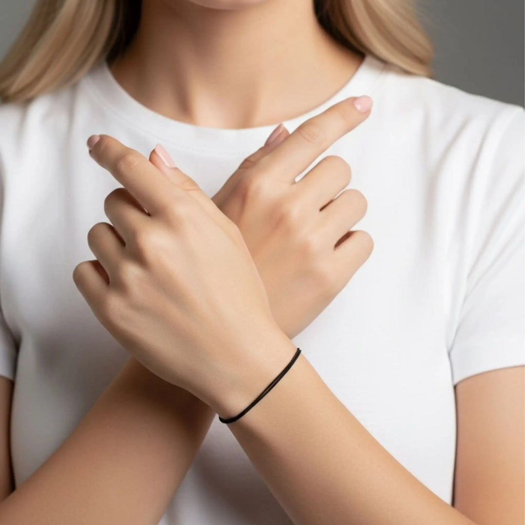 Close-up of a person wearing a white shirt with a black cord bracelet on their wrist.