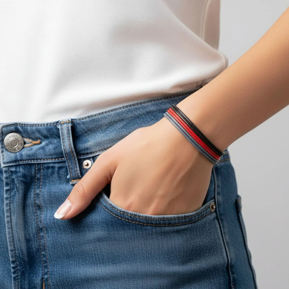 Person wearing blue jeans and a white shirt with a red and black bracelet on a gray background