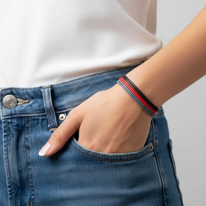Person wearing blue jeans and a white shirt with a red and black bracelet on a gray background