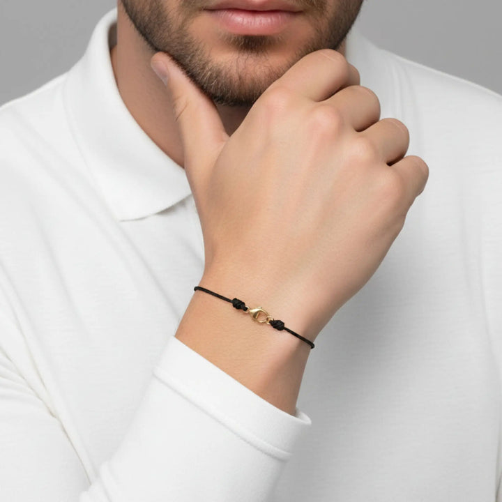 Man wearing a gold and black bracelet on his wrist, with a neutral background