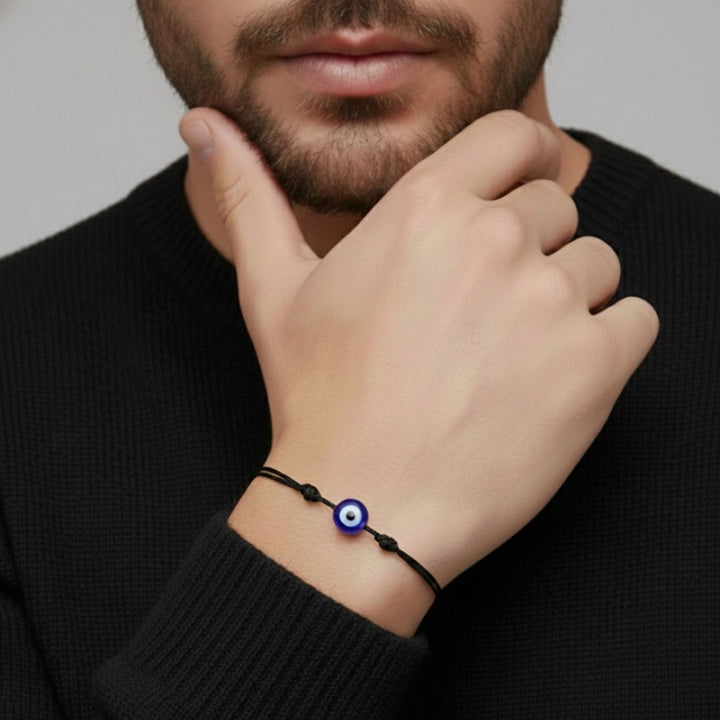 Man wearing a black bracelet with a blue evil eye charm on his wrist.