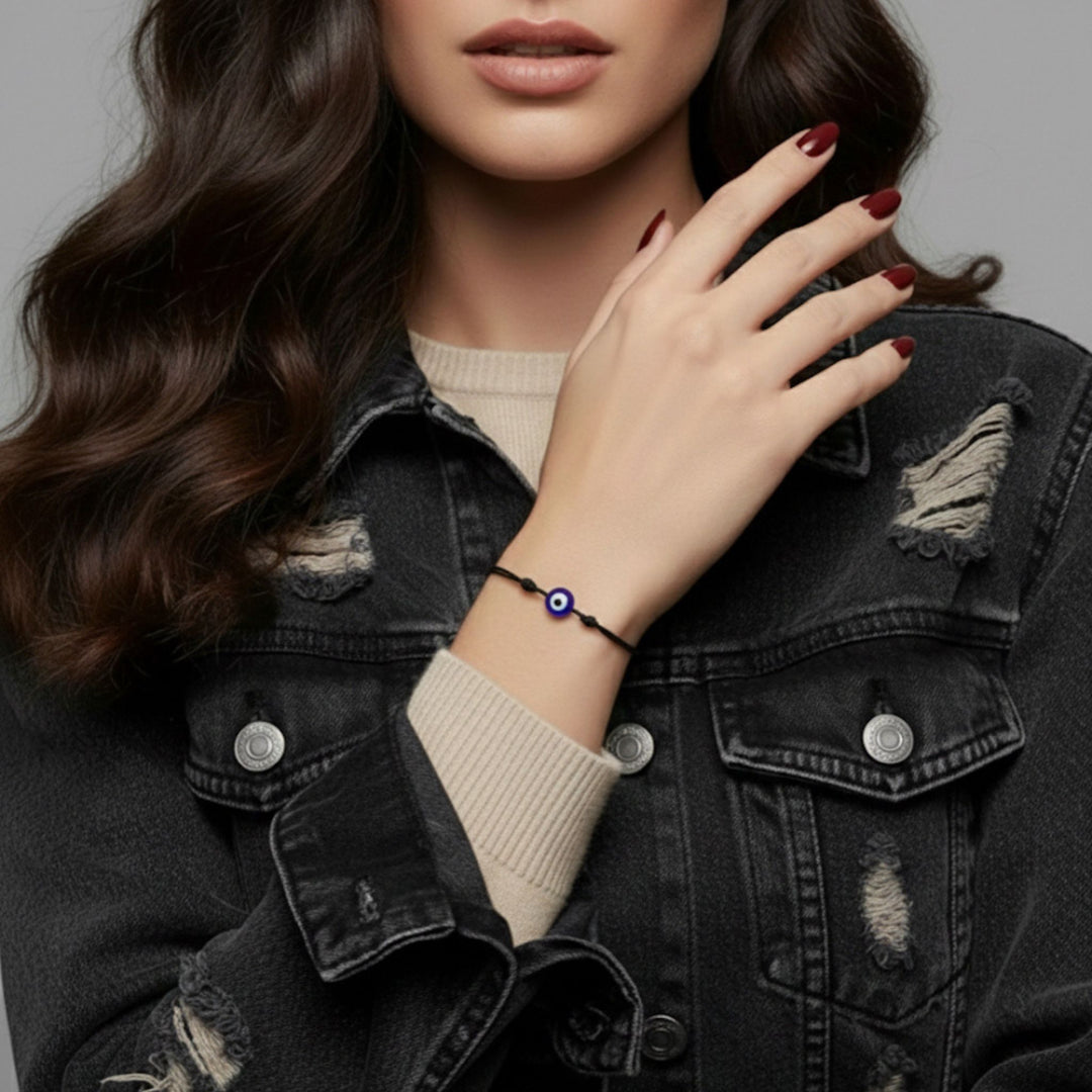 Woman wearing a black bracelet with a blue evil eye charm on a gray background