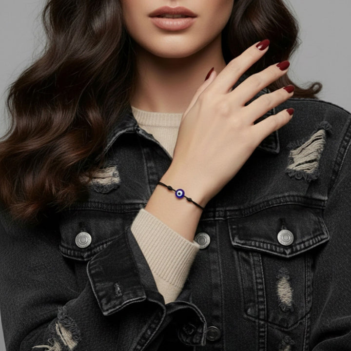 Woman wearing a black bracelet with a blue evil eye charm on a gray background